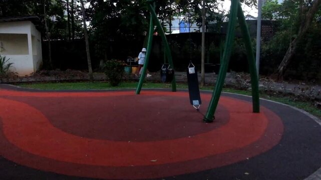 Empty park playground with red and black ground and swing set structures
