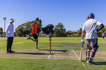 Obraz premium Diverse male cricket players bowling and batting on grassy field with stumps and helmet visible