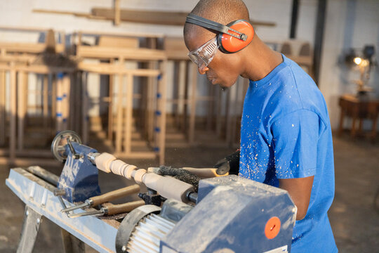 Woodworker shaping cylindrical wood blank on lathe in carpentry workshop, wood shavings scattering