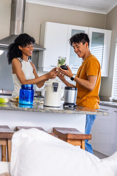 Diverse couple assembling blender cup with leafy greens at granite kitchen island, passing lid