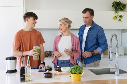 Family parents with teenage son preparing green smoothie and chopping vegetables at kitchen island