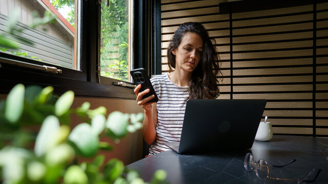 Woman working remotely using phone and laptop
