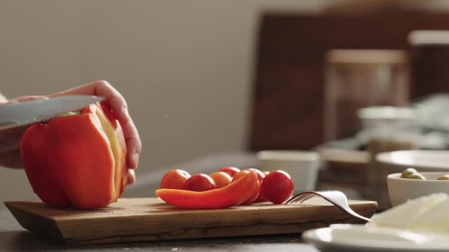 Close-up of red bell pepper being sliced on wooden cutting board with cherry tomatoes