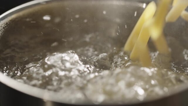 penne pasta falls in saucepan with boiling water