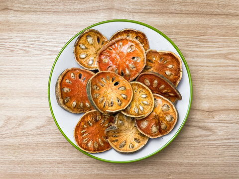 Slices of dried bael (matum) in a white plate on a wooden surface. A natural ingredient for making Thai herbal tea, infusions, and healthy drinks.