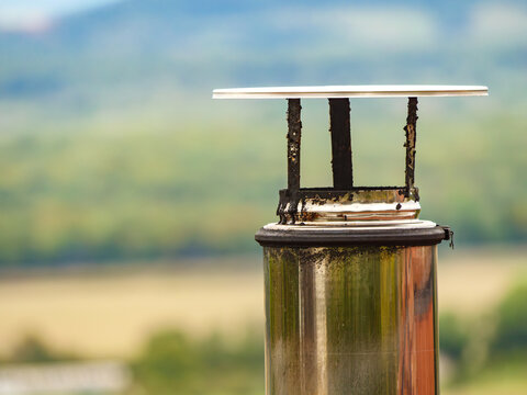 Chimney cap on a metal pipe in a rural area during daylight hours with blurred green background