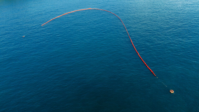long red oil containment boom deployed in a curved shape on the surface of deep blue ocean water for environmental protection and marine spill response.