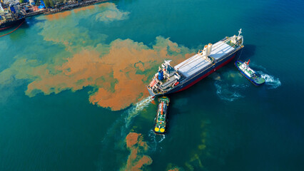 chemical spill or oil leak spreading from a large cargo ship and tugboats into the blue ocean, representing a severe water pollution crisis and marine environmental disaster. © Yellow Boat