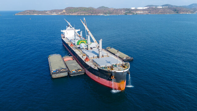 large bulk carrier ship transferring dark bulk cargo like coal or minerals into smaller barges alongside it in the open sea, representing maritime logistics and global supply chain.