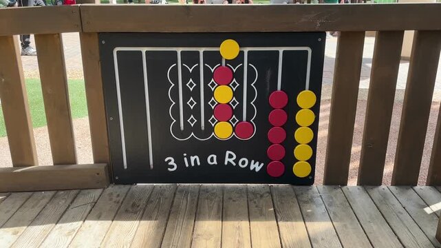 Three in a row game board mounted on wooden fence with colorful sliding discs for outdoor playground entertainment