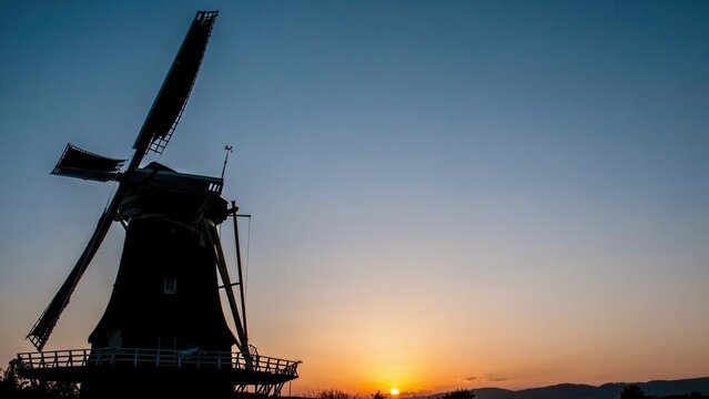 Silhouette of a traditional Dutch windmill against a sunset sky