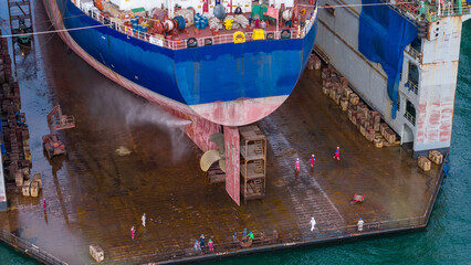 cargo ship's hull and propeller in a dry dock, undergoing high-pressure water cleaning and maintenance, highlighting maritime engineering and ship repair operations. © Yellow Boat
