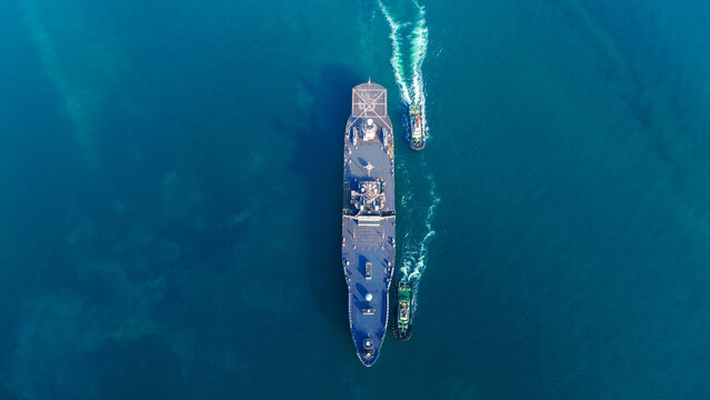 Nuclear power naval warship maneuvering near a port with assistance from tugboats, showcasing its flight deck and sophisticated sensor arrays, symbolizing maritime security and naval presence.
