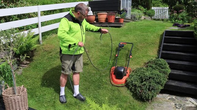 man coiling up an electric wire in the garden