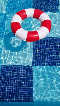 Hello summer, summer vacation, tourism, travel concept. A retro style red and white inflatable ring floats on the clear, sparkling water of a blue tiled swimming pool.  Space for text. 