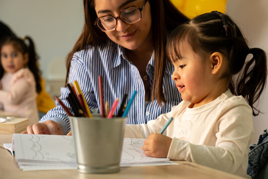 Teacher and young student drawing and learning together in a kindergarten classroom