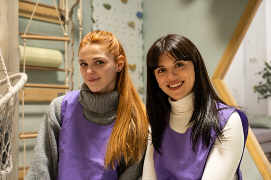 Two women wearing purple aprons smiling at the camera in a childcare facility