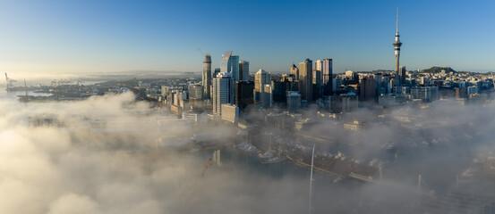 Naklejka premium Auckland, New Zealand - Early morning fog blankets the city skyline and harbor, revealing the Sky Tower and surrounding skyscrapers.