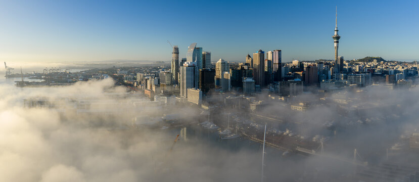 Auckland, New Zealand - Early morning fog blankets the city skyline and harbor, revealing the Sky Tower and surrounding skyscrapers.