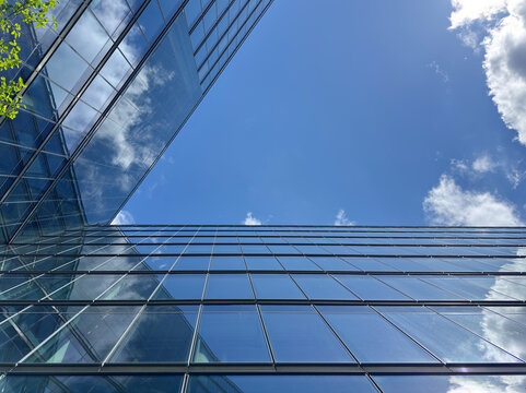 Looking up between two modern glass office buildings to a blue sky with clouds reflected in the windows