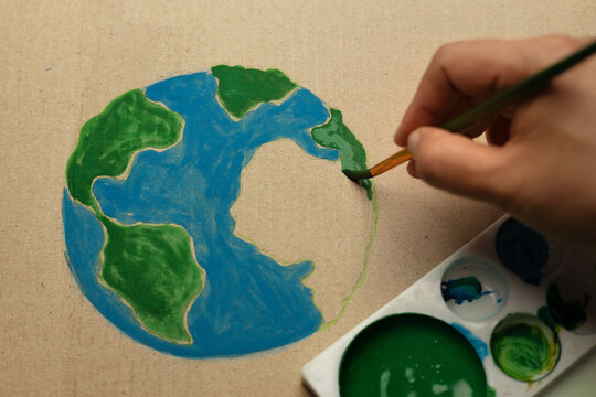 Earth Day painting activist concept with hand painting globe on cardboard, eco creativity