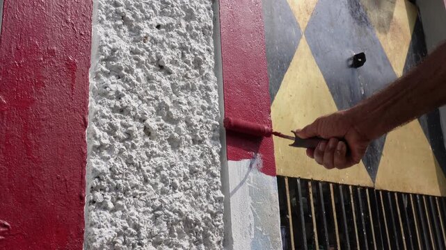 Worker painting textured wall with vibrant red roller