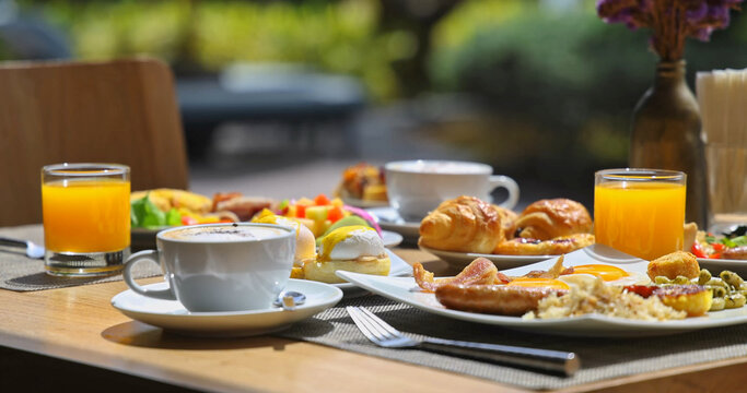 Gourmet breakfast spread sitting on wooden table at outdoor restaurant terrace, including coffee, orange juice, eggs benedict and pastries, bright morning sunlight, luxury travel lifestyle, hospitalit