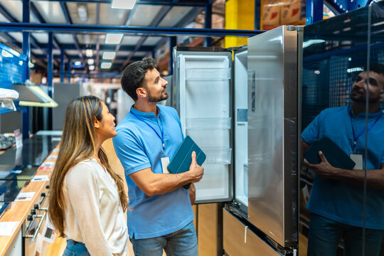 Sales assistant showing refrigerator to female customer in appliance store