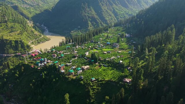 Aerial view of Himalayan village, orchards, river, and forested mountains in Parvati Valley, India, near near Sar Pass Trek, Kasol, Himachal Pradesh, India.