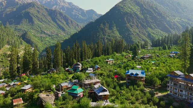 Drone flyover of Grahan Village surrounded by lush orchards, traditional mountain homes, and tall conifer forests in the Parvati Valley near Sar Pass Trek, Kasol, Himachal Pradesh, India.