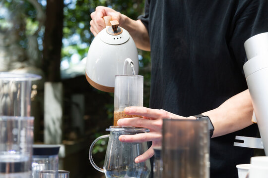 屋外のコーヒースタンドでコーヒー粉にお湯を注ぐ男性の手元