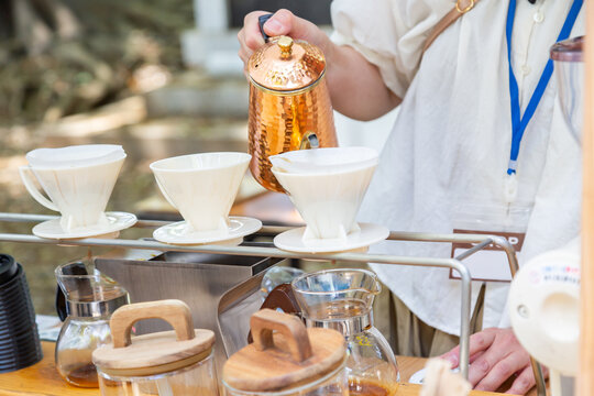 屋外のコーヒースタンドでドリッパーにお湯を注ぐ店員の手元、ドリップコーヒーをいれるカフェ店員　バリスタ