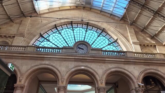 Low angle view of classic clock and large arched glass window under roof of historic Gare de l'Est train station in Paris, France