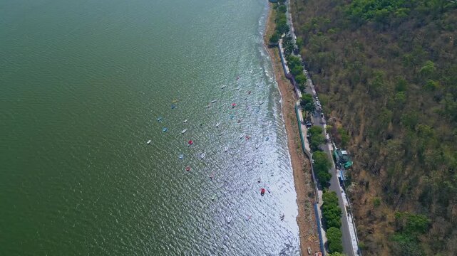 Cinematic orbit drone shot around the Boat Club shoreline in Upper Lake Bhopal featuring anchored boats lakeside road hillside landscape and sparkling waters in Madhya Pradesh India