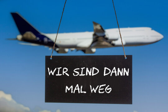 Symbolbild Betriebsferien: Schild mit der Aufschrift WIR SIND DANN MAL WEG vor einem startenden Flugzeug