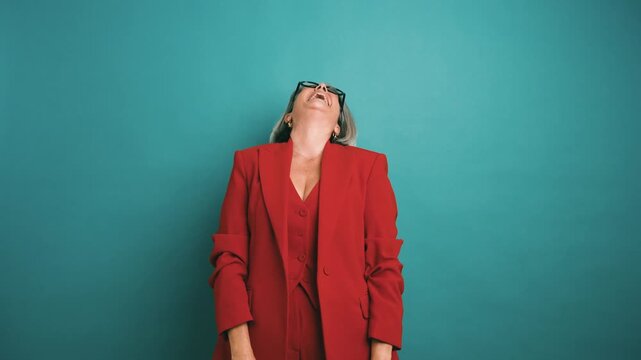 Cheerful mature woman with grey hair and glasses, wearing a vibrant red suit, laughing out loud and expressing genuine happiness and fun