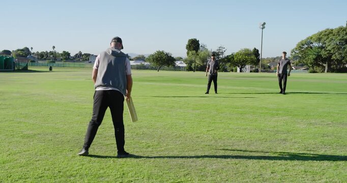 Teen male cricket team training on grass batsman swinging bat at incoming ball, fielder catching