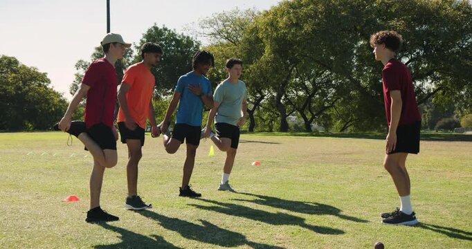 Indian coach leading diverse male players, doing quad, hamstring stretch, rising around cones