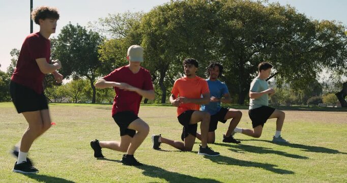 On whistle diverse male team lunging across orange cones reversing walking finishing warmup