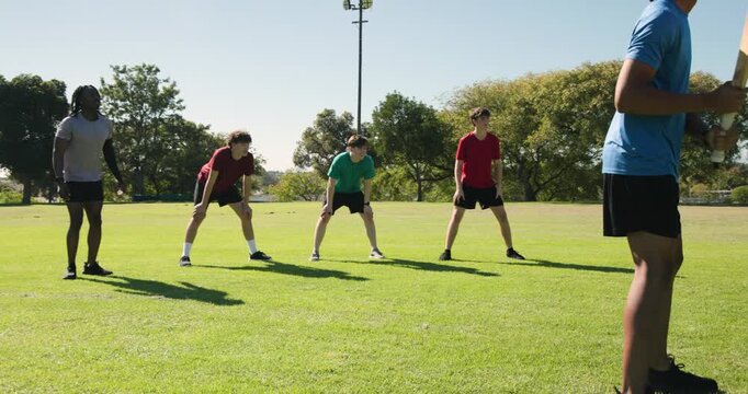 Coach passing ball underhand diverse male team in sportswear rotating catching drill on field
