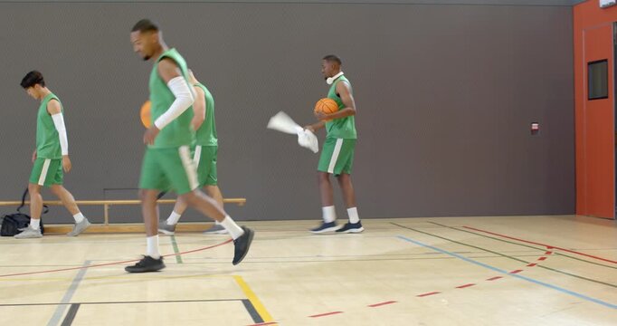 Entering school gym, diverse men in green jerseys dribbling balls preparing for basketball practice