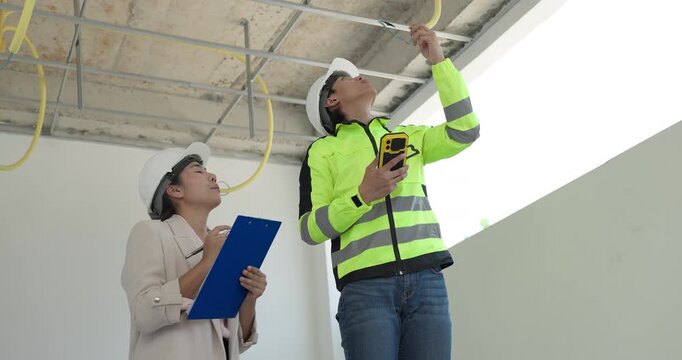 Site engineer and interior designer inspect exposed wiring and ceiling framework at a residential construction site, checking electrical readiness and coordinating renovation work before finishing.
