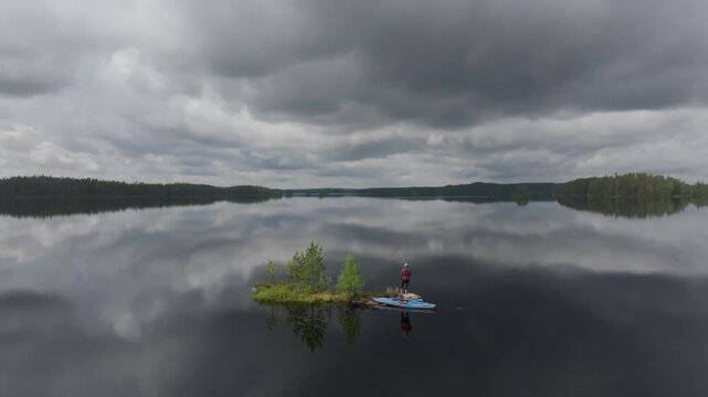 A lone kayaker takes a break on a tiny, secluded island in the middle of a calm wilderness lake. Aerial view of outdoor recreation and active lifestyle in Mujej&auml;rvi, Finland.