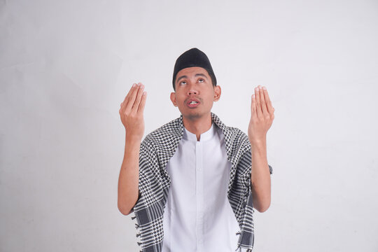 Young smiling happy Asian Muslim man in Arab costume kifaya, pecis with praying gesture facing upwards isolated on white background. Muslim people