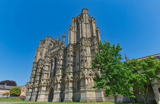 An upward view of a historic stone cathedral with intricate Gothic architecture and spires against a bright blue sky - Wells Cathedral - Wells - Somerset - UK