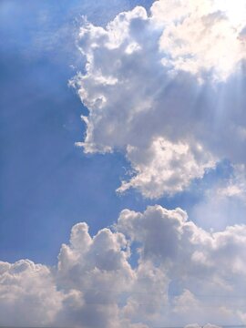 Beautiful blue sky background with fluffy white cumulus clouds and bright sun rays shining through