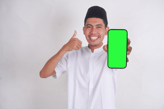 Muslim Asian man showing smartphone green screen with laughing, smiling, shocked and excited expressions. Muslim man in muslim costume, pecis standing smiling and pointing to blank mobile phone.
