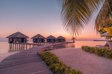 Fototapeta premium Amazing Maldives overwater villas sunset. Wooden jetty toward luxury water bungalows. Romantic tropical resort seascape glowing dusk. Inspire summer travel holiday backdrop ocean beach coastal evening