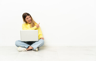 Young woman with a laptop sitting on the floor pointing back