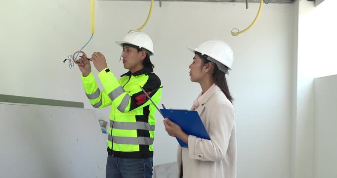 Site engineer and interior designer inspect exposed wiring and ceiling framework at a residential construction site, checking electrical readiness and coordinating renovation work before finishing.
